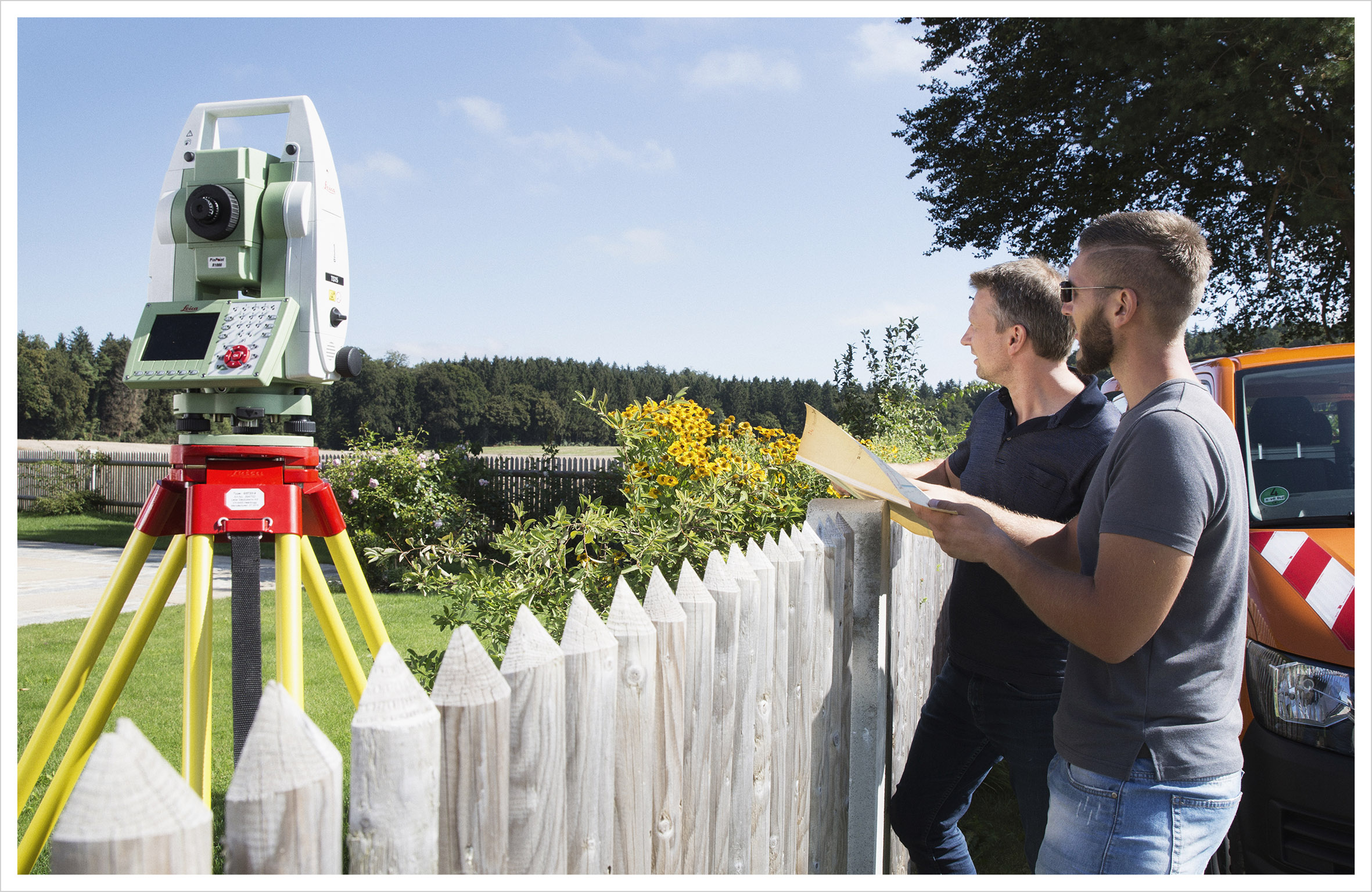 Zwei Vermessungsingenieure bei der Arbeit. Sie stehen an einem Gartenzaun und betrachten ihr Vermessungsobjekt